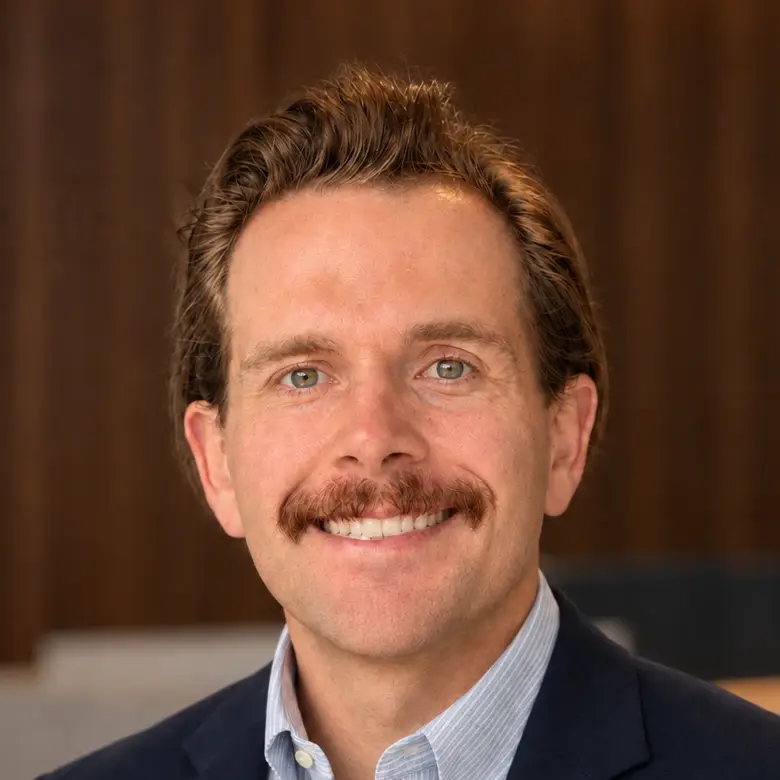 Michael Maxwell, smiling, in a navy blazer and a light blue striped shirt